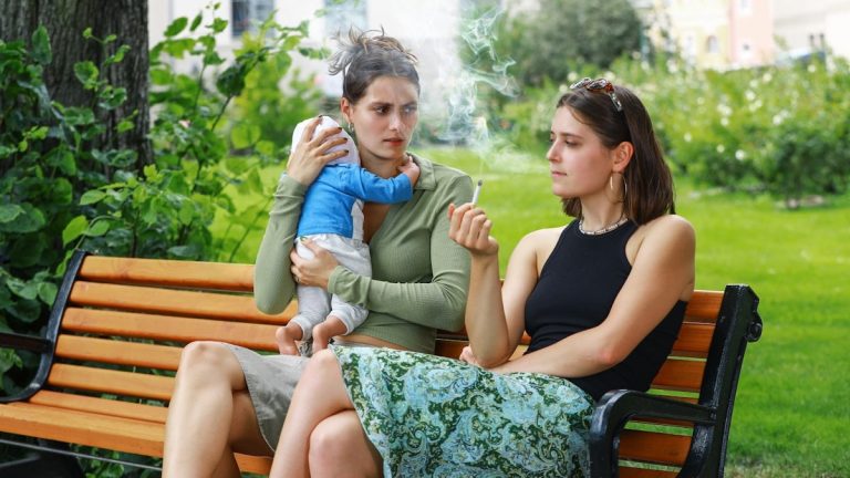 A girl smokes a cigarette on a park bench and disturbs her friend, a young mother and her baby, with her smoke – an appeal for a little more attention and awareness when smoking outdoors. Eine junge Frau raucht auf einer Parkbank eine Zigarette und belästigt mit ihrem Rauch ihre Freundin, eine junge Mutter mit ihrem Baby – ein Aufruf zu etwas mehr Rücksicht und Achtsamkeit beim Rauchen im Freien.