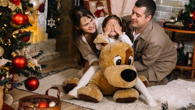 A man and a woman sitting on the floor with a large teddy bear